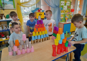 Pięcioro chłopców stoi przy stole i prezentuje wykonane przez siebie wieże według własnych pomysłów.