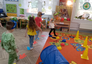 Grupka dzieci skacze po kolorowych śladach dinozaura.