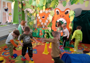 Grupka dzieci porusza się po półkolach i ścieżce sensorycznej, w tle widoczne elementy toru przeszkód: tunel, pachołki.