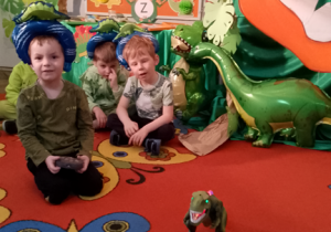 Bartek na dywanie prezentuje dzieciom swojego dinozaura.