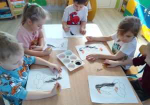 Grupa dzieci maluje czarną farbą pingwina.
