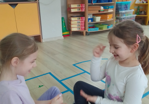 Zuzia i Lena siedzą naprzeciwko siebie i grają w „Kamień, nożyce, papier”.