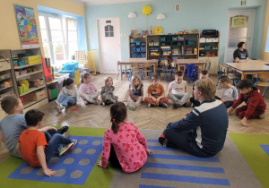 Dzieci z grupy Słoneczek słuchają słów instruktora siedząc w kółku na dywanie