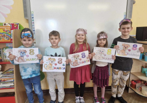 Karol, Eryk, Anastazja, Zosia i Franek stoją przed tablicą multimedialną. Dzieci trzymają w dłoniach kolorowanki.