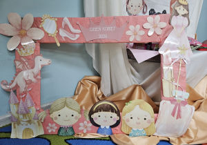Zdjęcie przedstawia bajkową foto ramkę z twarzami dziewczynek, księżniczką, smokiem, zamkiem, pantofelkami i napisem Dzień kobiet 2024.