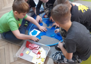 Zabawa klockami Dienesa - pięcioro dzieci siedzi wokół obręczy i wybiera klocki niebieskie zgodnie z kodem umieszczonym na kartoniku.