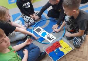 Zabawa klockami Dienesa - grupka dzieci wyszukuje klocki według kodu uwzględniając kolor, kształt i wielkość.