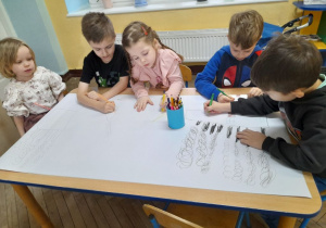 Pięcioro dzieci siedzi przy stole i rysuje na wspólnym kartonie różne rodzaje dymów.