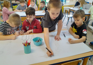 Dzieci siedzą przy stołach i rysują na wspólnych kartonach różne rodzaje dymów.