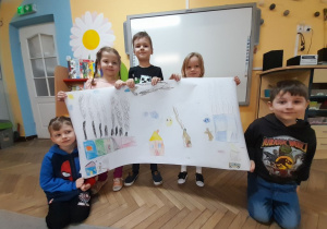 Samuel, Wiktoria, Oskar, Łucja i Karol prezentują wykonany przez siebie plakat przedstawiający różne rodzaje dymów. W tle tablica multimedialna.