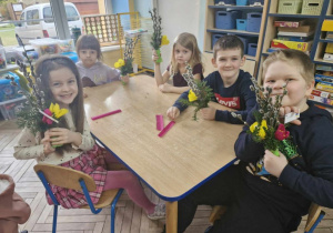 Julia, Zosia, Lenka, Franuś i Arek siedzą przy stoliku. Każde z dzieci trzyma w dłoniach wykonaną przez siebie wielkanocną palmę.
