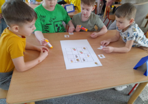 Karol, Arek, Filip i Eryk siedzą przy stoliku, na którym znajduje się sudoku obrazkowe. Chłopcy układają na planszy bajkowe obrazki.