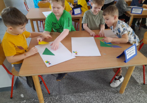 Karol, Arek, Filip i Eryk układają obrazki z elementów w kształcie figur geometrycznych według wzoru.