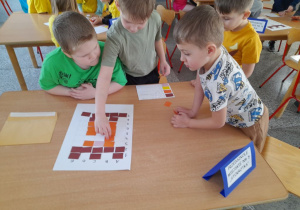 Chłopcy wykonują zadanie konkursowe przy stole - kończą układać wieżę Roszpunki na planszy zgodnie z podanym kodem.