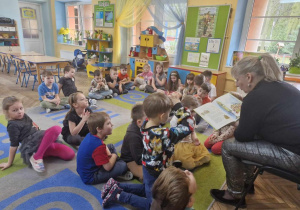 Dzieci z grupy "Słoneczek" siedząc na dywanie z uwagą słuchają opowiadania czytanego przez panią Ewę.