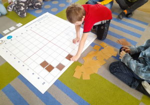 Tomek na podstawie podanych koordynatów układa na macie brązowe kwadraty.
