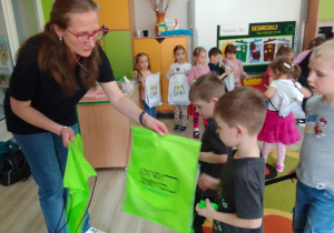 Przedstawicielka firmy PreZero Service Centrum wręcza dzieciom opaski odblaskowe i worki z logo firmy.