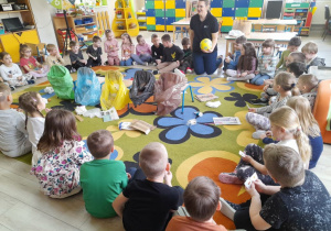 Dzieci z grupy "Biedronek" i "Słoneczek" siedzą w kole na dywanie razem z zaproszonym gościem. Na środku dywanu znajdują się worki na śmieci w różnych kolorach i rozrzucone śmieci.