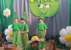 Chłopcy przebrani za zielone skrzaty stoją na tle dekoracji.