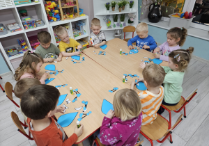 Przedszkolaki siedzą przy stoliku i wykonują pracę plastyczną "Uśmiechnięta kropelka".
