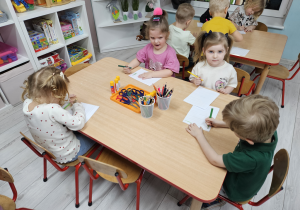 Klara, Oliwia, Oluś i Alicja siedzą przy stoliku kolorując kartki papieru.