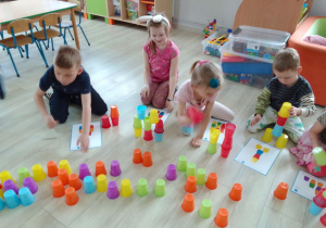 Dzieci układają wieże z kolorowych kubeczków według wzorów przedstawionych na kartkach