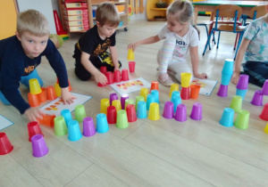 Kamil, Witek i Julia układają wieże z kubeczków według wzorów na kartach