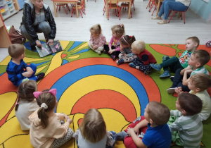 Dzieci siedzą w kole na dywanie, a Pani z biblioteki pokazuje im książkę o tematyce ekologicznej.
