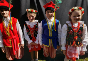 Czworo dzieci stoi obok sceny w parku Traugutta. Przedszkolaki ubrane są w stroje krakowskie.