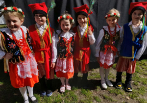 Sześcioro dzieci w strojach krakowskich pozuje do zdjęcia obok sceny w parku Traugutta.
