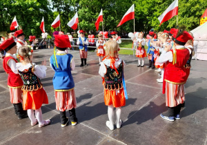 Dzieci w strojach krakowskich tańczą na scenie Krakowiaka. Przedszkolaki utworzyły duże koło.
