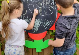 Dwoje dzieci rysuje motyle na tablicy w kształcie stokrotki.