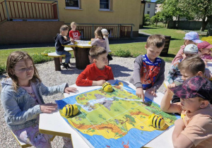 Grupka dzieci programuje pszczółki Bee Bot. Przed nimi leży mata do kodowania przedstawiająca mapę skarbów.