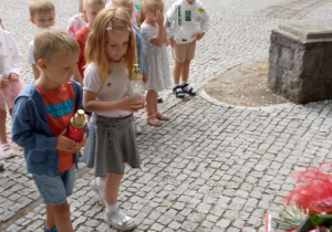 Emma i Wiktor niosą zapalone znicze. W tle przedszkolaki z grupy "Biedronki".