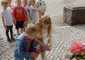 Dzieci stawiają zapalone znicze przed płytą upamiętniającą Żołnierzy Poległych w bitwie pod Kutnem.