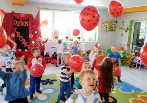 Dzieci w rozsypce na dywanie podrzucają czerwone balony w czarne kropki.