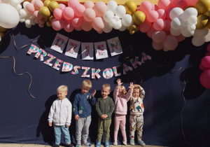 "Pszczółki" pozują do zdjęcia na tle napisu Dzień Przedszkolaka i kolorowych balonów.