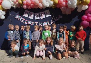 Dzieci z "Biedronek" stoją na tle dekoracji na Dzień Przedszkolaka.