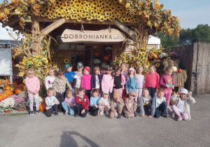 Dzieci stoją przed wejściem na farmę dyń udekorowanym kwiatami, liśćmi, dyniami. Nad dziećmi napis "Dobronianka".