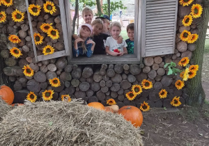 Sześcioro dzieci pozuje do zdjęcia w drewnianym okienku ozdobionym kwiatami.