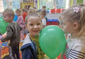 Szymek i Ola tańczą trzymając się za ręce. Między dziećmi widać zielony balon.