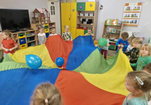 Przedszkolaki trzymają w dłoniach chustę animacyjną, na której podskakują niebieskie balony.