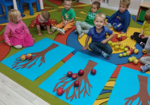 Grupka "Pszczółek" pozuje do zdjęcia, na dywanie jabłka ułożone na jabłonkach.