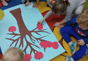 Maluchy podczas układania papierowych jabłek na sylwecie drzewa.