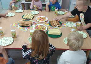 Grupka "Pszczółek" podczas poczęstunku siedzi przy wspólnym stole.