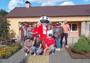 Pracownicy firmy Kellanova pozują do wspólnego zdjęcia. W środku stoi Pan Pringles, a obok niego Pani dyrektor. W tle budynek przedszkola.