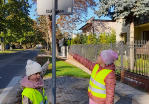 Dwie dziewczynki wskazują znak drogowy "Przejście dla pieszych".