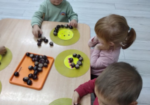 Wojtek, Jagoda i Tymek układają kasztany wokół buźki.