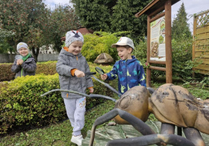 Olek i Wojtek Z. z lupami w rączkach oglądają rzeźbę mrówki. W tle widać Wojtka K.