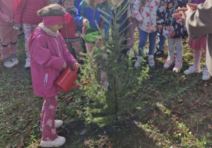 Klara i Wiktoria z konewkami w dłoniach podlewają zasadzone drzewko.